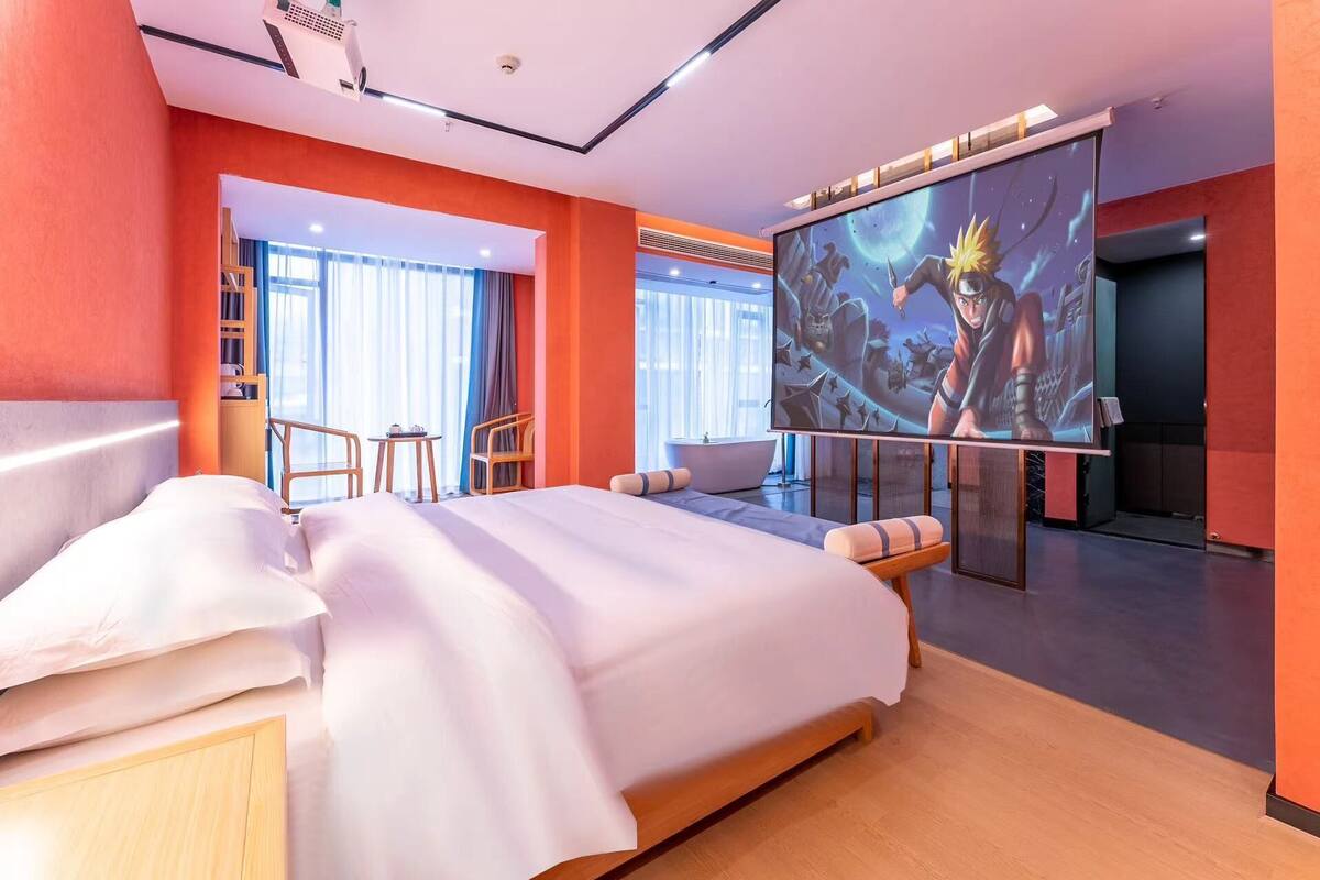 Una habitación de hotel moderna con una cama grande, una zona de estar con una mesa y sillas, una bañera y una pantalla grande mostrando una película con temática espacial.