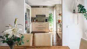 Moderni keittiö, jossa on vaaleat kaapit, ruokailutila puupöydällä ja -tuoleilla sekä roikkuva makrame-kasvi.
