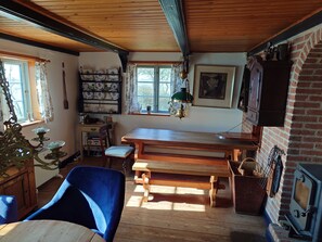 A rustic kitchen with wooden beams, a brick wall, a wooden table, a bench, a stove, and a window with curtains. - Historic holiday idyll close to the water (Faaborg)