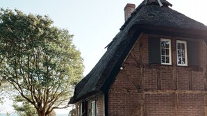 Ein rustikales Gebäude mit Strohdach, Backsteinmauern und einem Steinweg, der zu einer Bank führt.