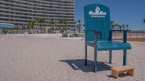 Una cadira de platja i una banca de fusta en una platja sorrenca, amb un hotel al fons.
