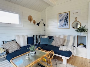 A cozy cabin interior with a blue sofa, a small table, and a hanging lamp. - Holiday home with views of the Little Belt (Haderslev)