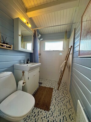 Une salle de bain comprenant des toilettes, un lavabo, un miroir et un espace douche.