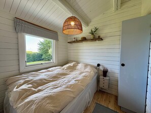 Une chambre à coucher avec un lit, une fenêtre, un luminaire suspendu, une table de chevet et une porte.