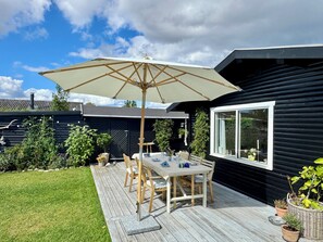 Une terrasse en bois avec une table et des chaises, un parasol et des plantes en pot.