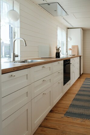 Een moderne keuken met witte kasten, een houten aanrecht, een inbouwoven en een raam met uitzicht.