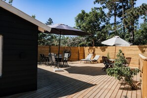 A wooden deck with outdoor furniture, including chairs and a table, and a large umbrella providing shade. - Lovely holiday home for the whole family (Vig)