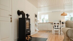 Ein Zimmer mit Kamin, Holzboden, weißen Wänden, einer Essecke mit Stühlen und einer hängenden Leuchte.