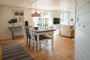 Een ruime kamer met een houten eettafel, witte stoelen, een televisie en een grote kast.