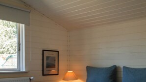 Ein Schlafzimmer mit Bett, Fenster, einem Wandbild und einer Nachttischlampe.