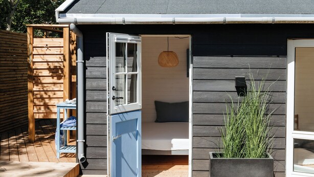 Eine offene Tür zu einem Zimmer mit einem Bett, einer Hängelampe und einem Blumentopf mit hohen Pflanzen.