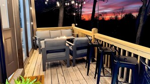 En terrasse med udendørs møbler, lyskæder og udsigt til solnedgang.