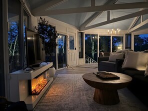 A modern living room with a fireplace, a sofa, a coffee table, and a view of the outdoors.