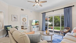 A living room with a ceiling fan, a television, a dining table, and a view of the outdoors. - Bright Beach Condo, Pool, Spa, Comfy Beds, Patio (St. Augustine)