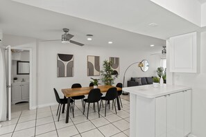 A modern kitchen with white cabinetry, a wooden dining table, black chairs, and a white countertop. - Swaying Palms Unit 2: Two Bedroom Retreat Near Beach, Heated Pool, Free Parking (Fort Lauderdale)