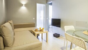 Een moderne woonruimte met een bank, een klein tafeltje met ontbijtartikelen, een televisie en een glazen tafel met stoelen.