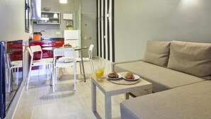Een moderne woonkamer met een bank, een eettafel met stoelen en een keukenhoek met een koelkast en een spoelbak.