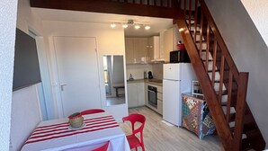 A compact kitchen with a dining area, wooden staircase, and a view into the living space. - Bright duplex near the beach - 4 guests (Villers-sur-Mer)