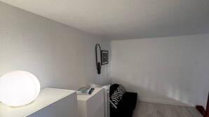 A room with a white desk, a standing fan, a black and white striped pillow on a black sofa, and a framed picture on the wall. - Bright duplex near the beach - 4 guests (Villers-sur-Mer)