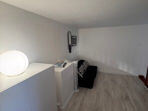 A room with a white desk, a standing fan, a black and white striped pillow on a black sofa, and a framed picture on the wall. - Bright duplex near the beach - 4 guests (Villers-sur-Mer)