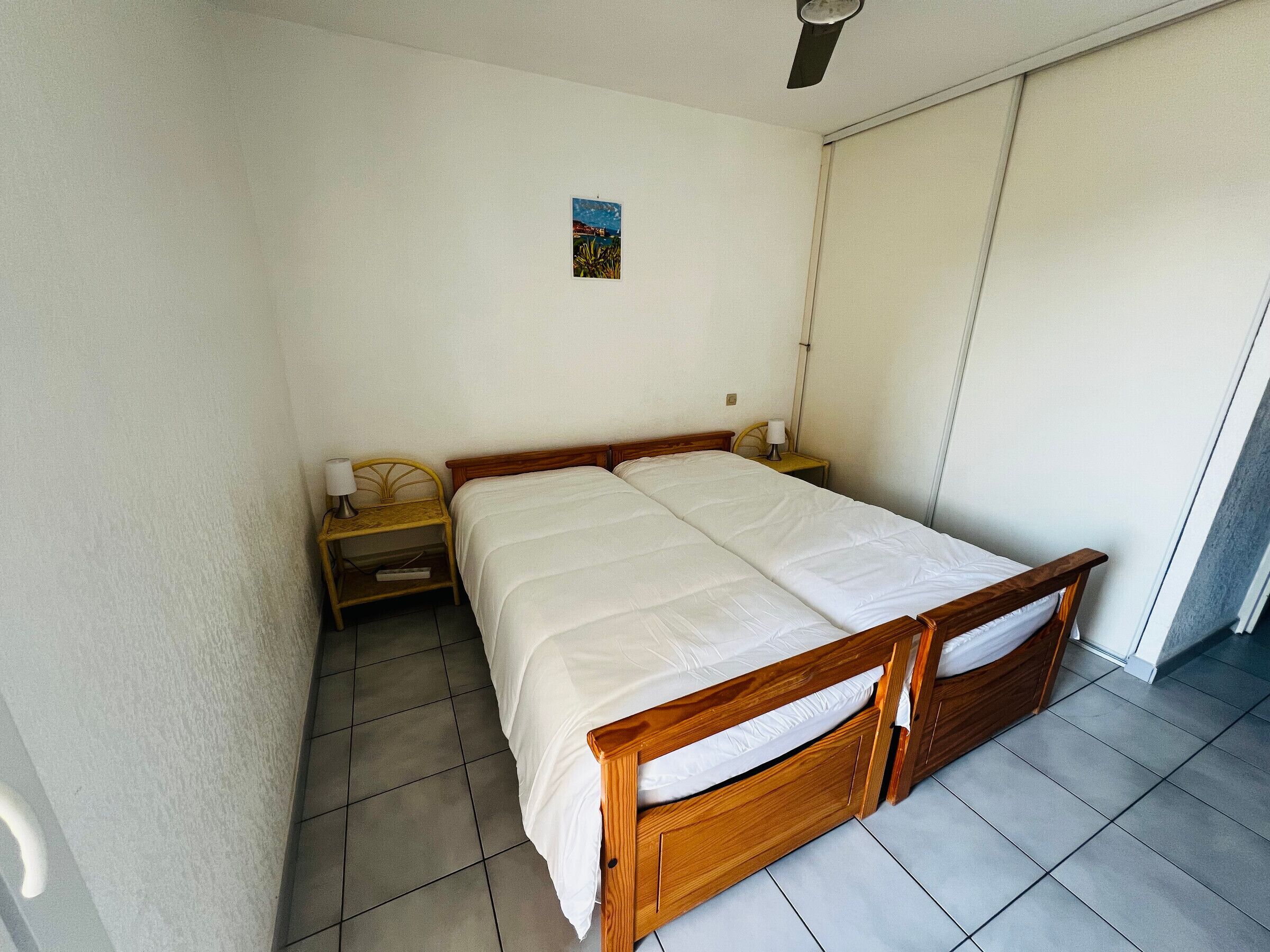Een kamer met een enkel bed, een houten frame, een klein nachtkastje met lamp en een schilderij aan de muur.