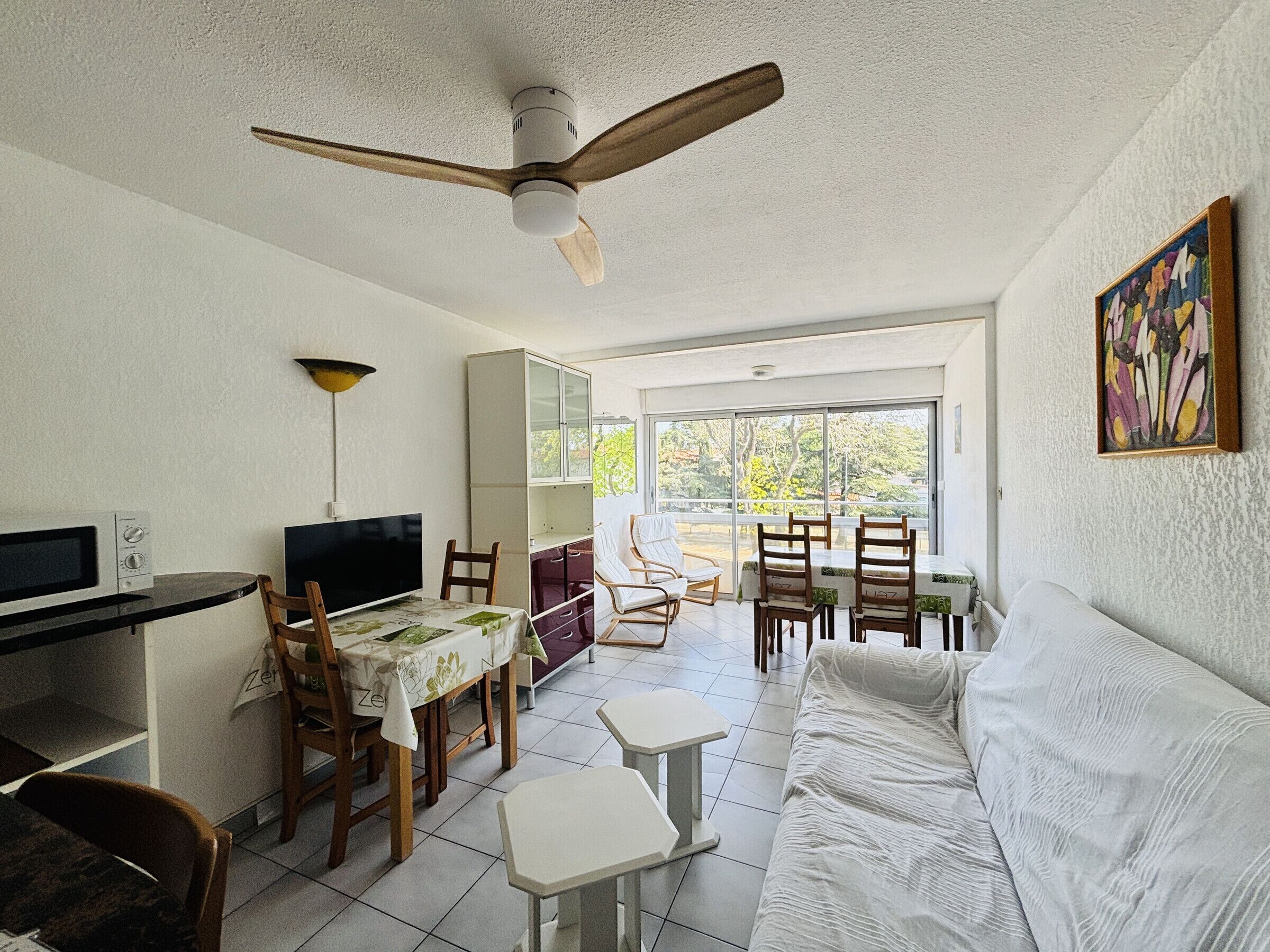 A living room with a ceiling fan, a dining area with a table and chairs, a sofa, and a TV.
