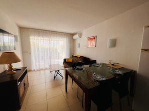 A dining area with a table set for four, a sofa with a yellow cushion, and a lamp on a cabinet. - Air-conditioned apartment near the beach - 4 guests (Argelès-sur-Mer)