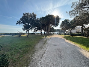 A gravel path leading through a grassy area with trees and a building in the background. - Air-conditioned apartment near the beach - 4 guests (Argelès-sur-Mer)