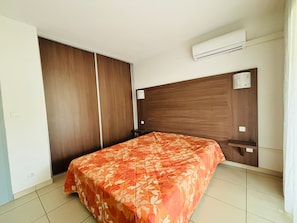 Quarto com cama, guarda-roupa, mesa de cabeceira e ar condicionado.