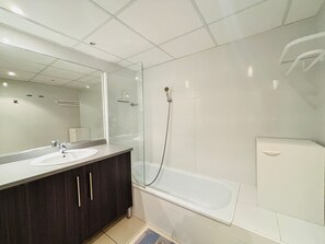 Un baño con lavamanos blanco, armarios de madera oscura, un espejo grande, cerramiento de ducha de vidrio y un inodoro blanco.