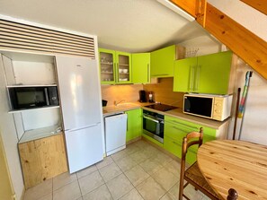 A compact kitchen with a refrigerator, microwave, stove, and a wooden dining table. - Cottage near beach, pets welcome - 4 guests (Bretignolles-sur-Mer)