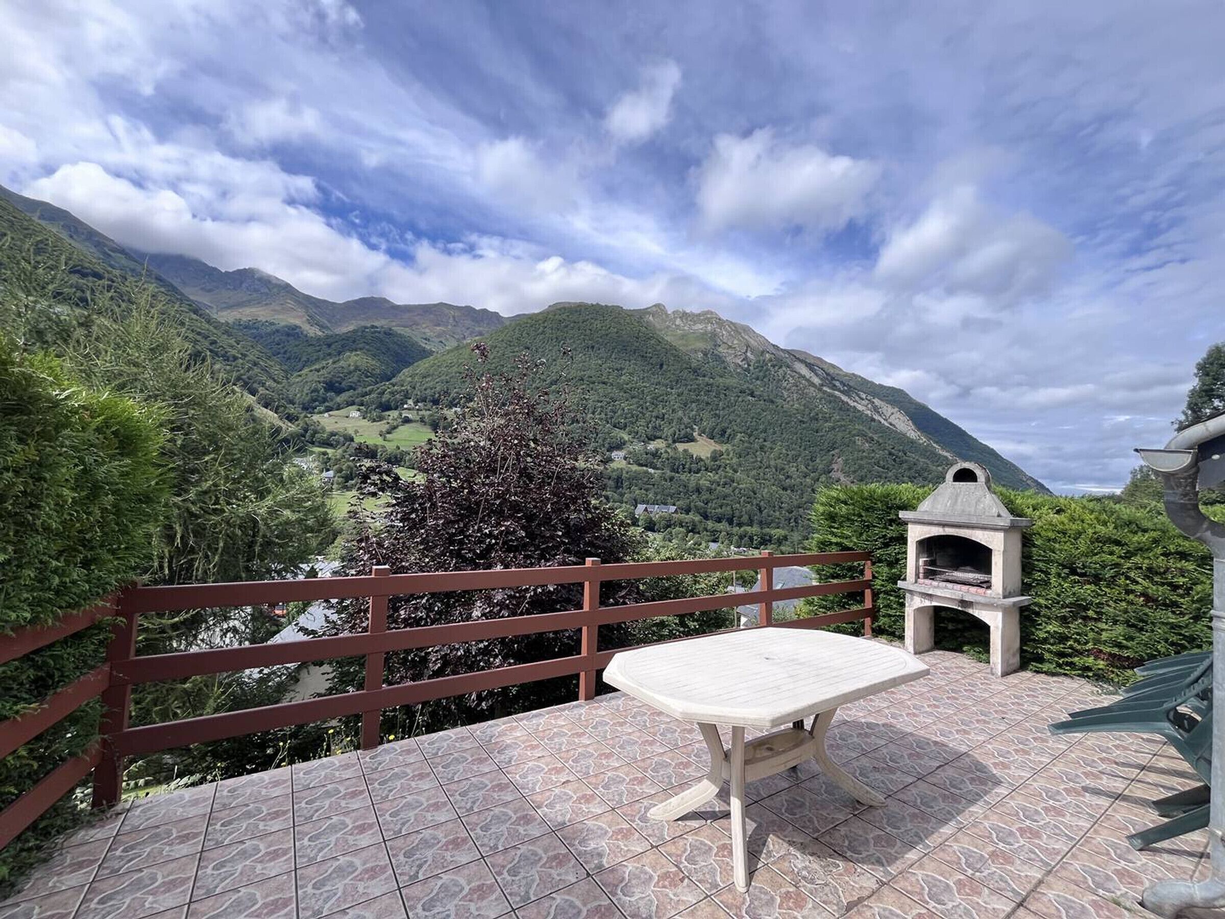 A patio with a table and a barbecue grill, overlooking a mountainous landscape.