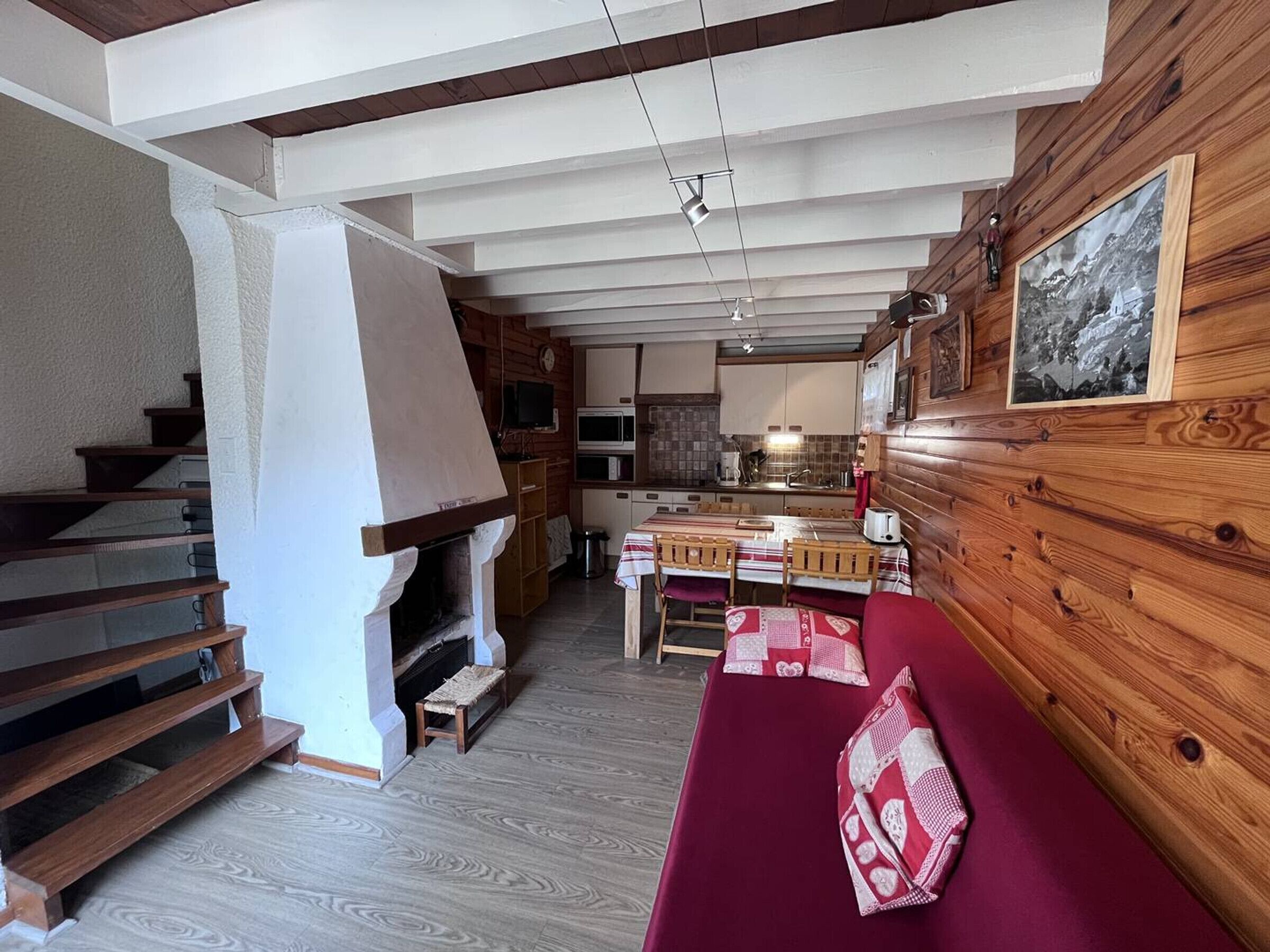 A cozy interior with a wooden staircase, a fireplace, a dining area, and a kitchen.