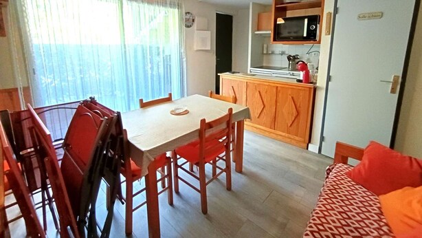 En kompakt opholdsstue med spisebord, stole, et tekøkken med mikroovn og en sofa.
