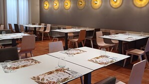 Un comedor con mesas dispuestas para dos, con posavasos de estampado de hojas y una fila de luces fijadas a la pared.