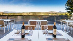 Un área de comedor al aire libre con mesas dispuestas para dos, cada una con una botella de vino y una copa.