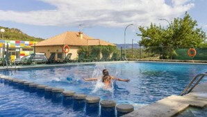 Una piscina con una persona nadando, un flotador salvavidas y un edificio con techo de azulejos al fondo.