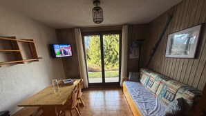 Una habitación con una mesa de madera, sillas, un sofá, un televisor y una puerta que da a un jardín.