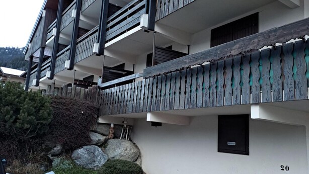 Un edificio de varios pisos con balcones, una pared de piedra y un cartel con el número 20.