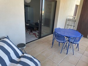 Un balcon avec une table et des chaises bleues, un canapé à rayures et une porte-fenêtre coulissante donnant sur un coin repas.