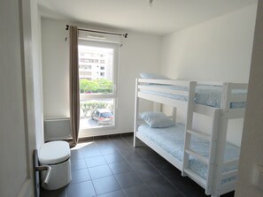 Una habitación pequeña y limpia con una cama nido, un inodoro y una ventana con vistas a un estacionamiento y edificios.