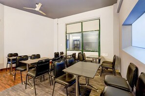 A conference room with tables and chairs, a ceiling fan, and a large window with green framing. - Deluxe Grace Complex (Chennai)