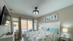 A bedroom with a bed, a nightstand, a desk, a ceiling fan, a window, and a wall sign. - Harbor Front Condo. Minutes to downtown. (Cape May)