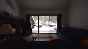 Una sala de estar con sofá, una mesa de centro, una lámpara, chimenea y un ventanal con vistas a un paisaje nevado.