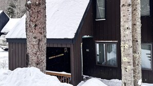 Una cabaña de madera con techo nevado, una puerta visible y una ventana.