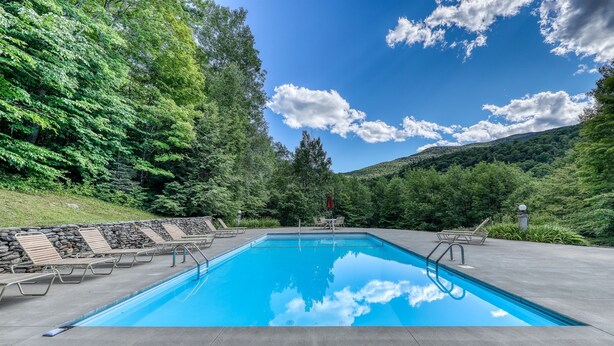 Una piscina con sillas de descanso y un muro de piedra.
