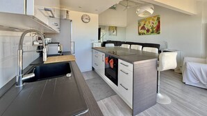 Una cocina moderna con horno empotrado, lavamanos con grifo flexible y comedor con mesa y sillas.