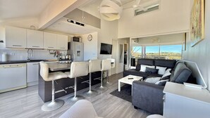 Una sala de estar moderna con sofá, sillas, una mesa de centro y una zona de cocina con armarios y electrodomésticos.