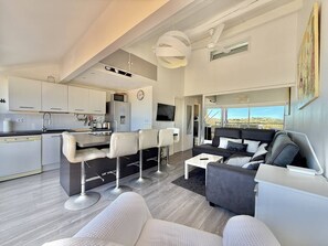 A modern living room with a sofa, chairs, a coffee table, and a kitchen area with cabinets and appliances. - CAP D'AGDE - Plage de la Roquille // Réf 0406 (CAP D AGDE)
