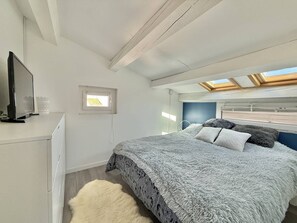 Ein Schlafzimmer mit einem Bett, einem Fernseher, einem Oberlicht und einem Fenster.